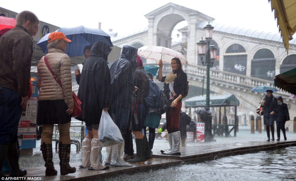 Tourists walk on footbridges near the Rialto bridge as heavy rain puts a dampener on their tour 
of the city