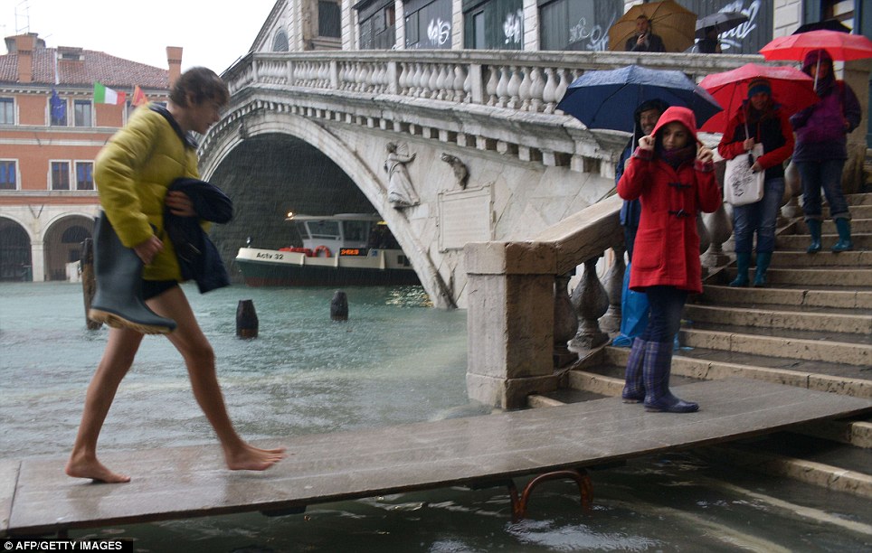 One tourist takes off their boots to walk on a makeshift footbridge in the rain