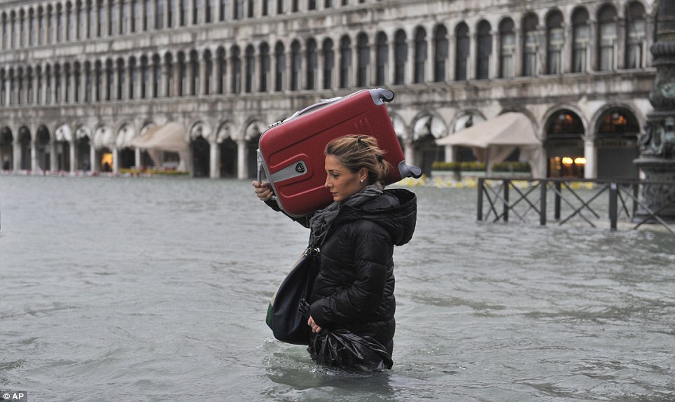 A tourist crosses flooded the iconic square carrying a suitcase on her shoulder while wading 
through the waters