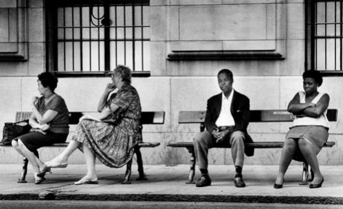 Whites sit on a bus stop bench with blacks two weeks after the city of Johannesburg in South Africa allowed blacks to travel on 'whites-only' buses in February, 1990.