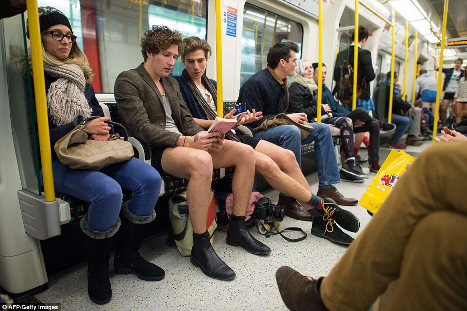 One man reads a book while his friend talks to him on the London Underground. A woman to their right seems less impressed 