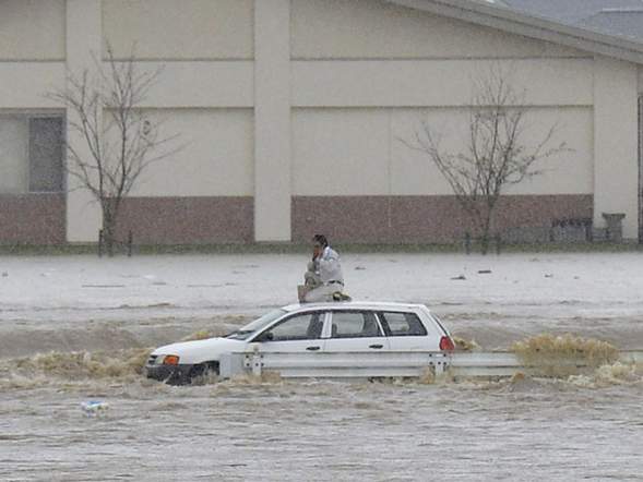 A man kneels on the roof of a car on a road flooded by the Kinugawa river, caused by typhoon Etau in Joso