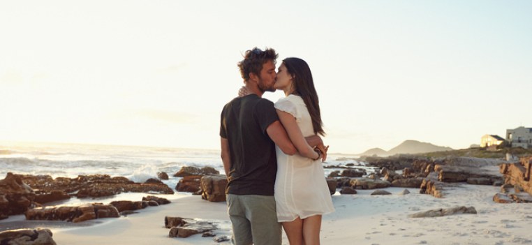 Outdoors shot of loving young couple kissing on the beach at sunset. Young man and woman in love on the sea shore in evening.